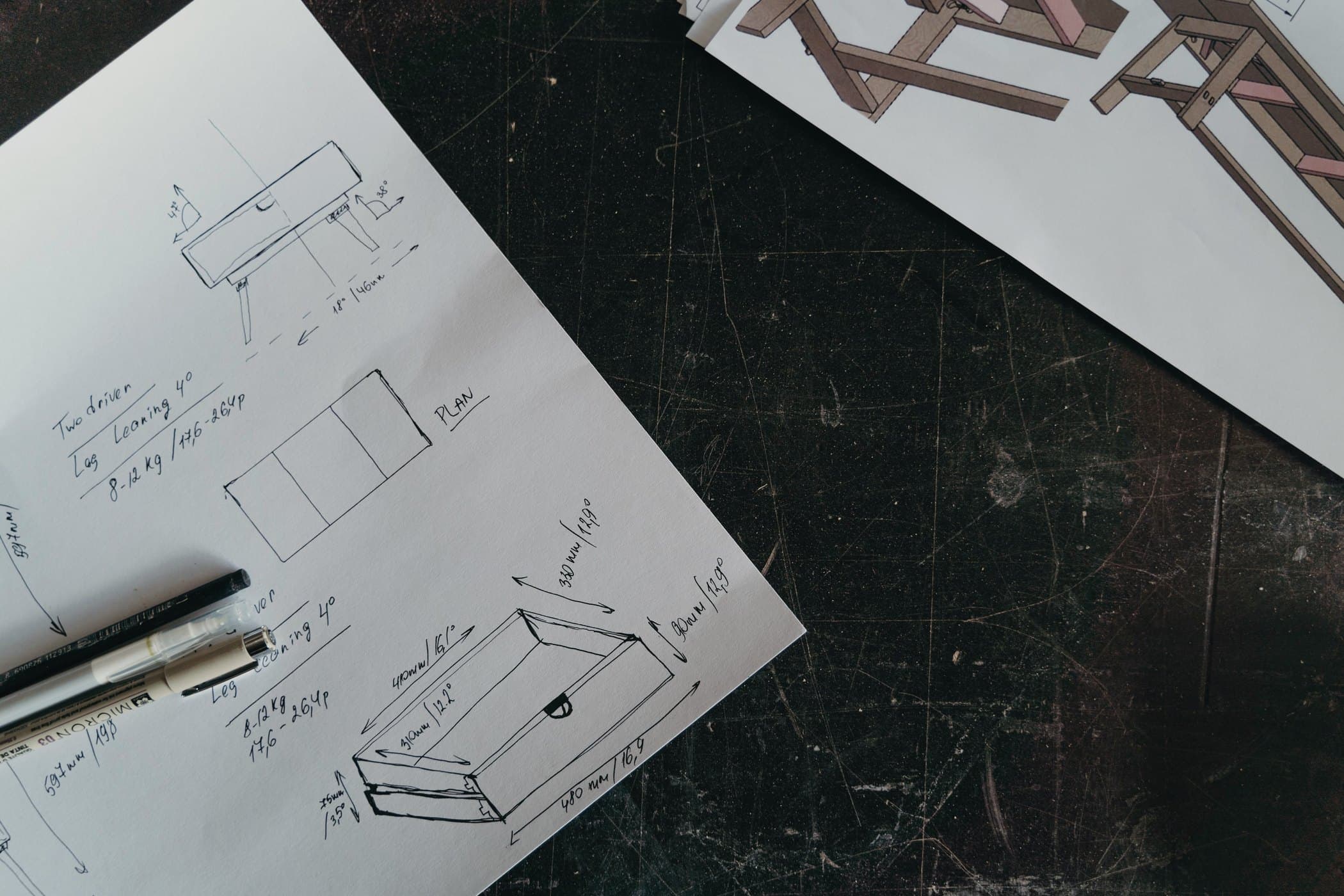 Pen sketches of a box with measurements in millimetres, on paper laid over a dark workbench