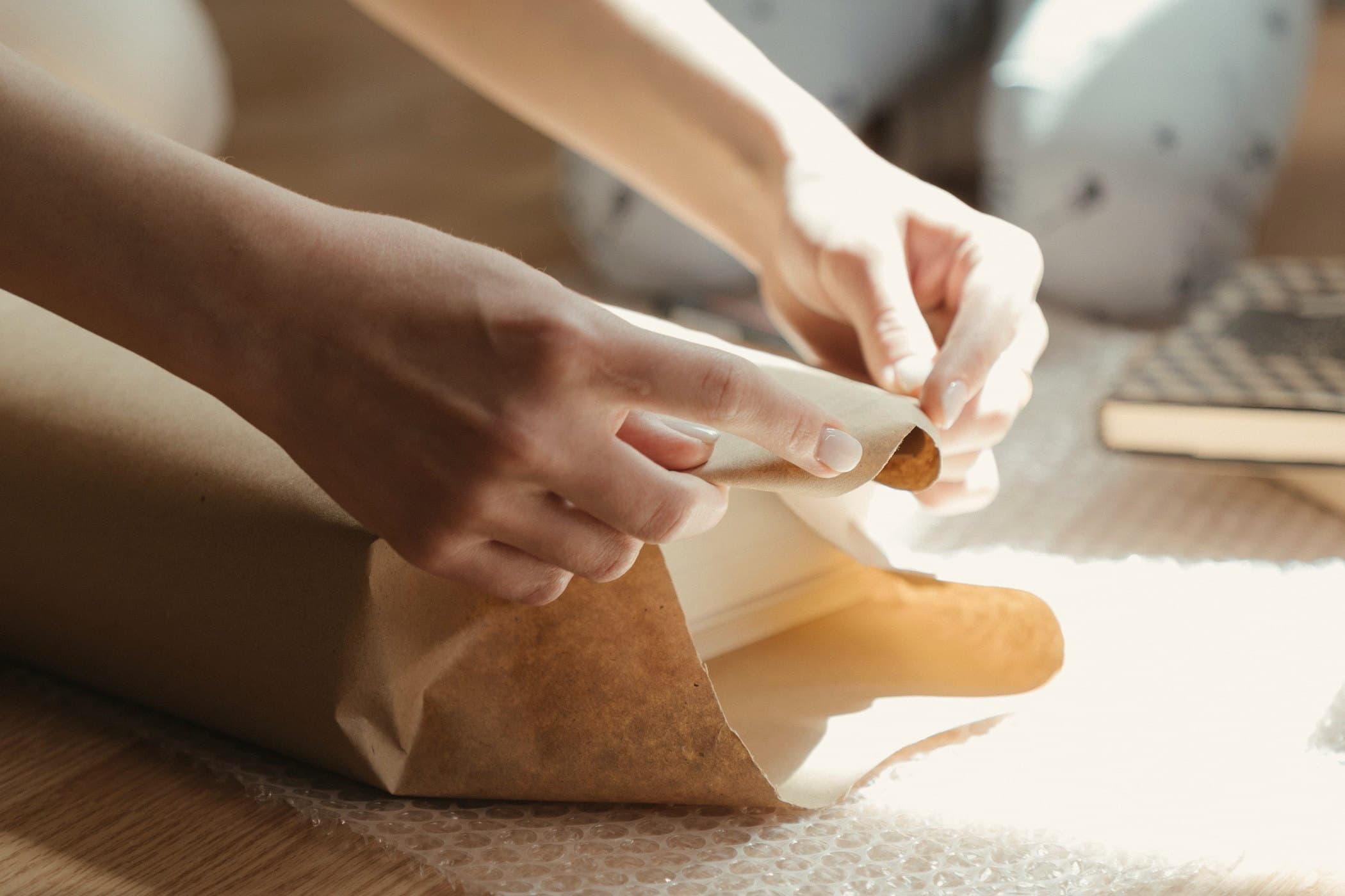 Hands folding brown kraft paper around a box in warm afternoon light